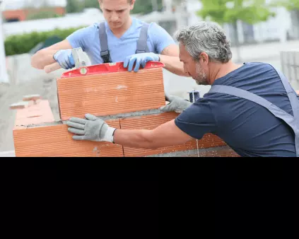 un artisan maçon cheveux gris et son jeune apprenti en train de monter un mur de parpaings