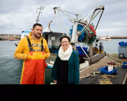 un pêcheur en ciré et une femme conseillère devant un bateau de pêche