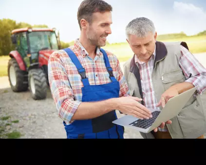 un jeune agriculteur en bleu de travail tenant un ordinateur erit un homme cheveux gris avec un tracteur en arrière-plan