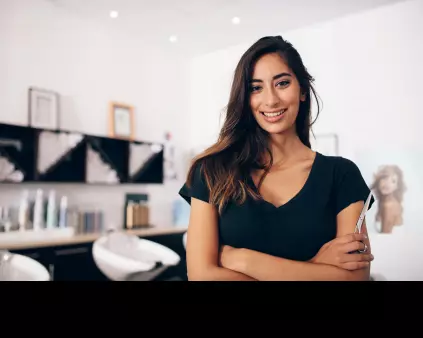 une jeune femme brune qui croise les bras devant des bacs dans un salon de coiffure