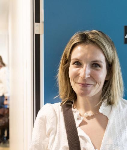 femme souriante blonde et portant une chemise blanche devant un mur bleu