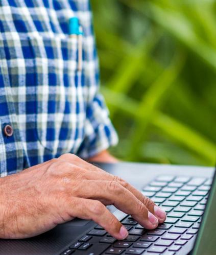homme chemise à carreau tenant un ordinateur portable dans un champ