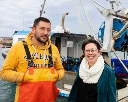 un pêcheur en ciré et une femme conseillère devant un bateau de pêche