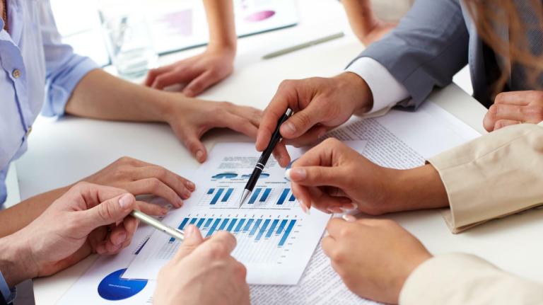 plusieurs mains de personnes autour d'une table qui montrent un document avec des graphiques