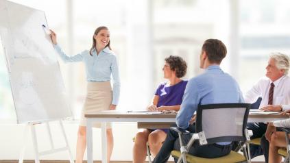 plusieurs personnes autour d'une table avec une femme debout à un tableau blanc