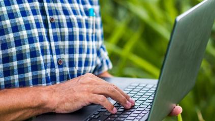 homme chemise à carreau tenant un ordinateur portable dans un champ